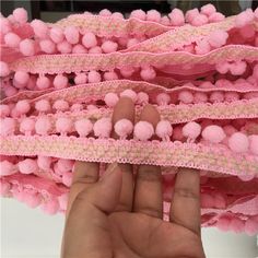 a hand is holding some pink pom - poms on a piece of lace