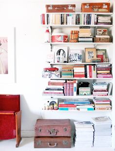 a book shelf filled with lots of books next to a red chair and two pictures on the wall