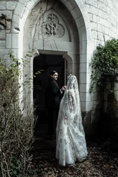 a bride and groom standing in front of an old church door with their veil draped over them