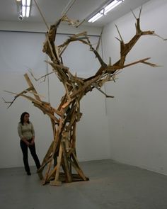 a woman standing in front of a sculpture made out of sticks and branches on display