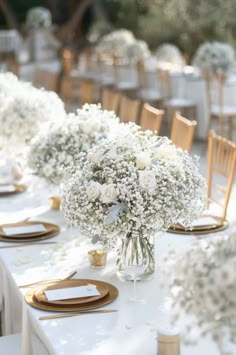 the table is set with white flowers and gold place settings