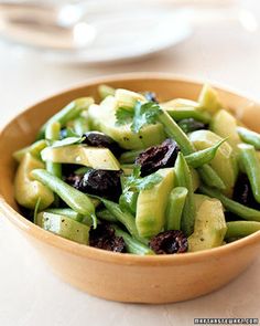 a wooden bowl filled with green vegetables on top of a white tablecloth covered table