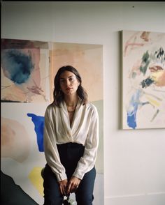 a woman sitting on top of a stool in front of paintings and holding a cane