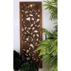 a wooden panel with leaves on it next to some potted plants and a planter