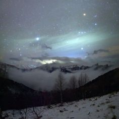 the night sky is filled with stars and clouds above some snow covered mountains in the distance