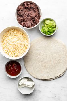 tortilla ingredients laid out in bowls on a marble countertop, including cheese, lettuce and sauces