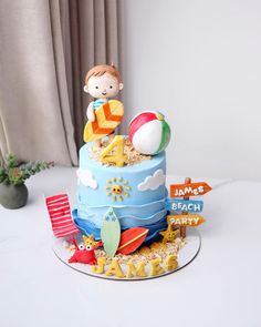 a birthday cake with a boy on top and beach signs in the middle, sitting on a table next to a potted plant