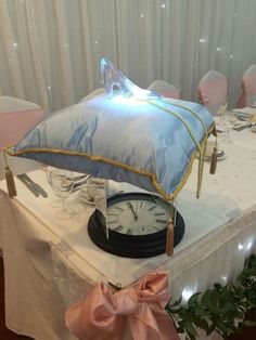 a clock sitting on top of a table next to a blue pillow and pink ribbon