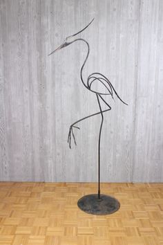 a metal flamingo standing on top of a wooden floor next to a white wall