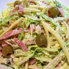 a salad with green olives and ham on it is in a white bowl, ready to be eaten