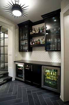 a home bar with black cabinets and marble counter tops is lit by a chandelier