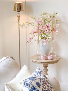 a table with flowers in vases on top of it next to pillows and a lamp