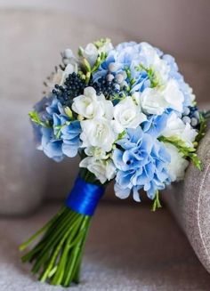 a bouquet of blue and white flowers is sitting on the arm of a couch in front of a chair