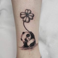 a panda bear with a clover tattoo on the ankle is sitting next to a four - leaf clover