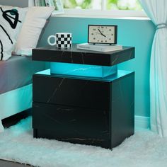 a nightstand table with a clock on it next to a bed and window in a bedroom