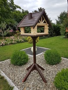 a wooden bird house sitting on top of a metal stand in the middle of a garden