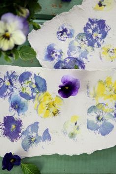 two pieces of paper with flowers painted on them next to some leaves and purple pansies