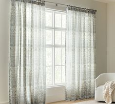 a white chair sitting in front of a window with curtains hanging on the windowsill