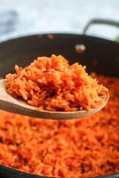 a wooden spoon full of cooked rice in a pan