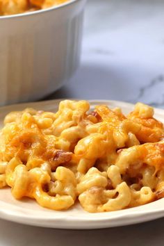 macaroni and cheese on a white plate next to a bowl of macaroni