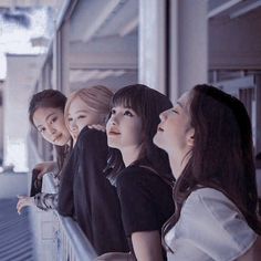 four young women are looking at something in the distance while sitting on a balcony railing