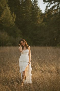 a woman in a white dress is walking through tall grass with trees in the background