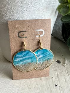 two blue and white earrings sitting on top of a card next to a potted plant