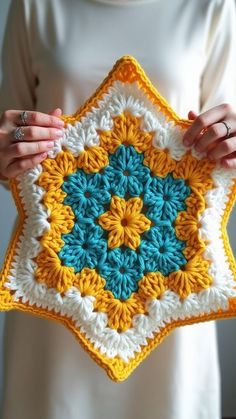 a woman is holding up a crocheted star with blue, yellow and white colors