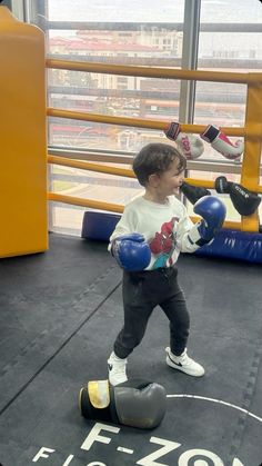 a young boy wearing blue boxing gloves standing on top of a punching bag in a gym