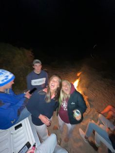 a group of people standing next to each other on a sandy beach at night with a fire in the background