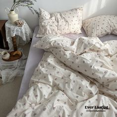 an unmade bed with white sheets and pink flowers on the comforter, next to a small potted plant