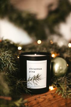 a candle sitting on top of a wooden table next to christmas ornaments and lights in the background