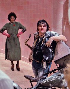 a man standing next to a woman with a snake on his arm and a motorcycle