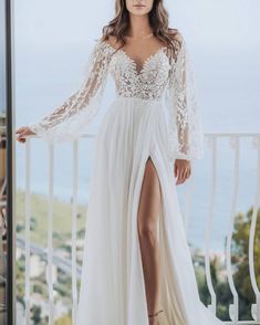 a woman standing on a balcony wearing a white dress with long sleeves and high slit