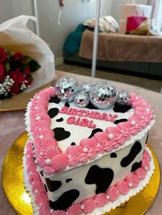 a heart shaped birthday cake with pink frosting and black dots on top, decorated with three silver hearts