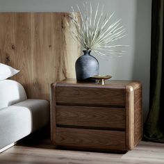 a bed with a wooden headboard and white pillows next to a plant in a vase