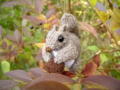 a stuffed squirrel is sitting on top of a tree branch with leaves around it and looking at the camera