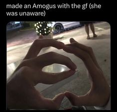 someone making a heart with their hands while standing on the side walk at night time