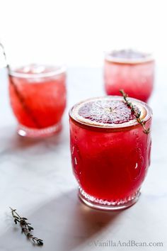 two glasses filled with red liquid sitting on top of a white table next to lavender sprigs