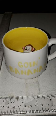 a yellow and white coffee cup with a monkey head in it's mouth on a ruler