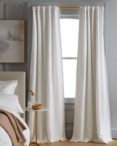 a white bed sitting next to a window covered in curtains