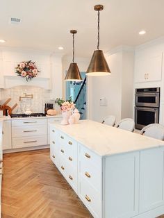 a large kitchen with white cabinets and gold accents on the counter tops, along with two pendant lights hanging from the ceiling