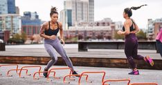 two women are running on the street near an obstacle course with city buildings in the background