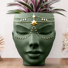 a green face planter with gold beads on it and a potted plant next to it