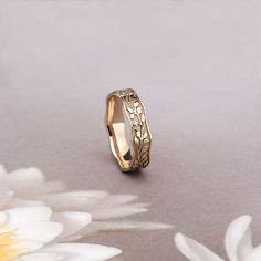 a gold wedding ring sitting on top of a flowered tablecloth with white daisies in the background