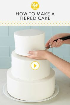 a woman is decorating a tiered cake with white frosting