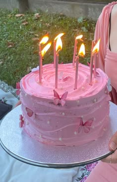 a pink cake with lit candles sitting on a silver platter in front of a woman