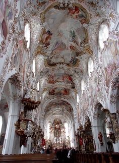 the interior of an old church with many paintings on the walls and ceiling, along with pews