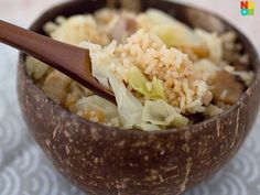 a wooden bowl filled with rice and meat on top of a white table cloth next to a brown spoon