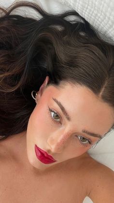 a woman laying on top of a bed with her hair blowing in the wind and wearing red lipstick